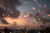 Romantic sunset sky with floating golden heart-shaped bokeh lights creating dreamy atmosphere for Valentine's Day, wedding, love celebration backgrounds.