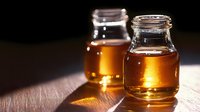 Golden honey in glass jars on wooden surface with warm sunlight creating amber glow and natural shadows for organic food photography and kitchen decor.