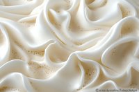 Creamy white whipped texture with golden sparkles creates luxurious waves and folds, suggesting rich dessert topping or cosmetic cream background for food or beauty industry.