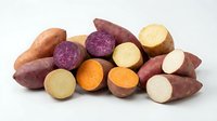 Colorful sweet potato varieties with vibrant orange, purple and white flesh displayed whole and sliced on white background for healthy cooking recipes.