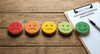 Customer feedback evaluation concept with colorful emoji faces from sad to happy on wooden background with clipboard and pen for business rating.