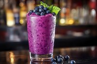 Vibrant purple blueberry smoothie in glass garnished with fresh berries and mint leaf on dark wooden bar counter with blurred bottles background.