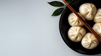 Steamed Asian dumplings baozi in black ceramic bowl with wooden chopsticks on light background, top view with copy space for menu design.