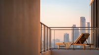 Modern wooden lounge chair on urban rooftop balcony with city skyline view at sunset, contemporary architecture and relaxation space design.