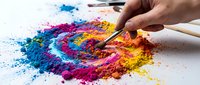 Paintbrush applying vibrant multicolored powder pigments in blue, pink, yellow, and orange hues on white surface for art, design, and creative projects.