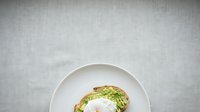 Avocado toast with poached egg on white plate against gray linen background, healthy breakfast food for culinary, recipe, and nutrition content.