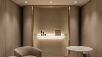Modern minimalist spa treatment room with beige walls, built-in shelving, ambient lighting, and comfortable seating for relaxation and wellness services.