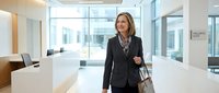 Professional businesswoman walking through modern corporate office lobby with glass walls and contemporary architecture for workplace presentations.