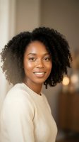 Young African American woman with natural curly hair smiling warmly in cozy cream sweater, soft indoor lighting for lifestyle and wellness content.