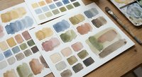 Watercolor paint swatches and color palette samples spread on wooden surface for artistic projects and creative design work.