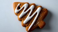 Festive gingerbread cookie in shape of Christmas tree with white icing decoration on gray background, holiday baking concept.