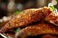 Crispy golden fried chicken pieces with crunchy coating and fresh herbs garnish on dark plate, soft bokeh background for food photography.