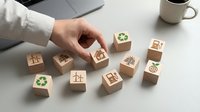 Hand selecting wooden cube with recycling symbol from collection of eco-friendly business icons on modern office desk for sustainable corporate strategy.