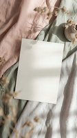 Blank white paper card on soft linen fabric with eucalyptus leaves and natural shadows. Minimalist mockup for branding, stationery, wedding invitations.