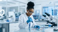 Young female scientist of African descent wearing white lab coat and blue gloves conducting research with microscope in modern laboratory setting for scientific research, education, and healthcare content.