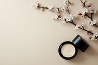 Luxury face cream jar with spring cherry blossom branch on beige background. Minimal flat lay composition for beauty and skincare product photography.