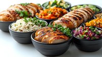 Grilled chicken breast slices served in black bowls with variety of sides including rice, roasted vegetables, and fresh salads on white background.