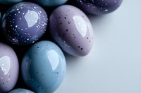 Pastel colored Easter eggs decorated with delicate speckles and dots in soft purple, blue and lilac shades on light background, creating festive holiday mood.