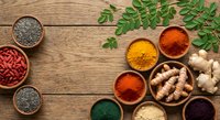Colorful spices and herbs in wooden bowls on rustic table with fresh moringa leaves, turmeric, paprika, ginger root creating natural cooking ingredient flatlay.