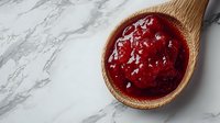 Fresh homemade strawberry jam in wooden spoon on marble surface. Sweet berry preserve for breakfast, baking and cooking recipes.