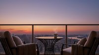 Luxury penthouse interior with two armchairs facing floor-to-ceiling windows overlooking cityscape at sunset, featuring modern furniture and panoramic urban skyline view for upscale lifestyle and real estate design.