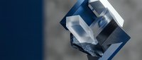 Clear crystal cube with geometric facets reflecting light on blurred background for luxury jewelry design and premium branding applications.