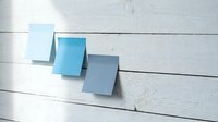 Three blank blue sticky notes on a white wooden wall, perfect for reminders, planning, and organization concepts.