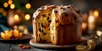 Traditional Italian panettone Christmas bread with candied fruits and raisins, sliced to show fluffy texture, on wooden table with warm holiday lights bokeh background.