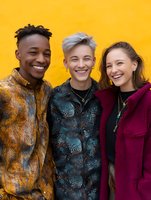 Diverse group of young friends laughing together against vibrant yellow wall, wearing colorful trendy jackets and expressing genuine joy and connection.