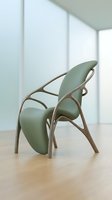 Modern sage green lounge chair with curved wooden frame displayed in bright minimalist interior space with natural light from windows.
