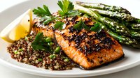 Grilled salmon fillet with black pepper crust served on quinoa bed, garnished with fresh herbs and asparagus spears on white ceramic plate.