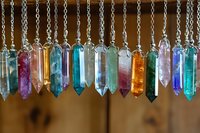 Colorful crystal pendants hanging in row against brown background, featuring amethyst, quartz, and other healing stones for spiritual and jewelry design.