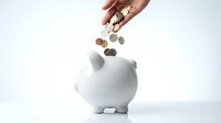 Hand dropping coins into white ceramic piggy bank on clean background for savings and financial planning concepts.