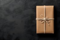 Gift box wrapped in kraft paper with elegant white string bow on dark textured background. Minimalist holiday or birthday present styling with copy space.