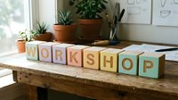Wooden alphabet blocks spelling WORKSHOP arranged on a rustic table in a bright creative studio with plants and sketches in background.