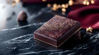 Dark chocolate candy with golden sparkles on black marble surface, elegant confectionery photography with bokeh lights and burgundy fabric in background.