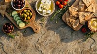 Mediterranean appetizer platter with olives, feta cheese, crackers and fresh herbs on rustic stone surface for entertaining and gourmet dining.