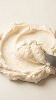 Creamy whipped frosting or buttercream spread with a spatula on neutral background, ready for baking and cake decorating projects.