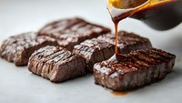 Grilled beef steaks with barbecue sauce being poured, perfectly cooked meat with char marks on white surface for culinary and restaurant marketing.