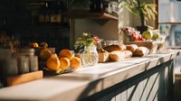 Cozy kitchen counter with fresh oranges, bread, flowers and natural sunlight streaming through window creating warm homey cooking atmosphere.