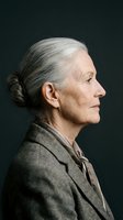 Mature woman with gray hair styled in a bun, wearing a gray blazer, photographed in profile against a dark background. Suitable for senior lifestyle, business, and corporate projects.