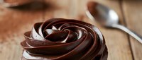 Rich chocolate frosting swirl on wooden surface with spoon, decadent dessert topping for cakes and cupcakes, sweet confectionery delight for baking projects.