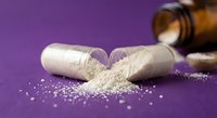 Opened capsules spilling white powder on purple surface with amber bottle in background for pharmaceutical and supplement industry applications.
