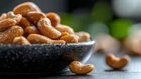 Fresh roasted cashew nuts in black ceramic bowl with natural light and blurred background, macro food photography showing texture and details of healthy snack.
