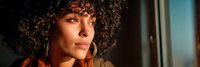 Young African American woman with curly hair and gold hoop earrings in warm natural lighting creating dramatic shadows and highlights on her face.