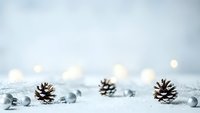 Winter holiday background with pine cones and silver ornaments on white surface with warm bokeh lights creating festive Christmas atmosphere.