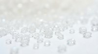 Clear glass beads scattered on white surface with shallow depth of field, suitable for jewelry design, craft projects, and decorative product photography.