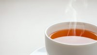 Steaming hot tea in white ceramic cup with saucer on light background. Warm beverage with rising steam for relaxation and comfort concepts.