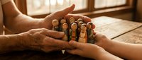 Hands protecting wooden peg doll family figures representing care, security, family protection, insurance concepts and community support in warm lighting.