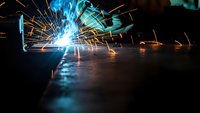 Professional welder creating bright sparks during metal fabrication work in industrial workshop with protective equipment and safety gear.